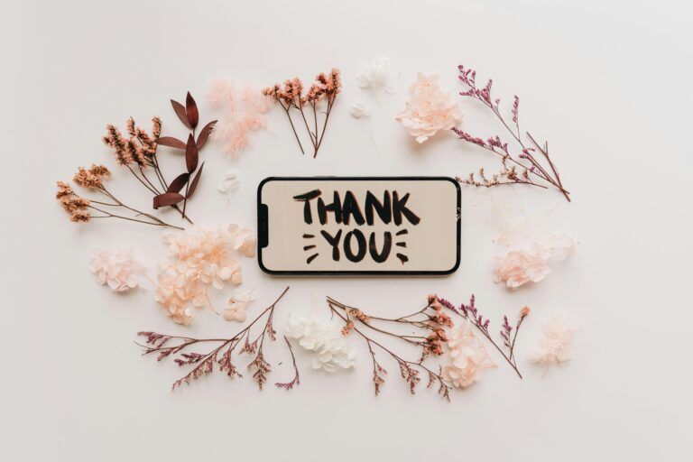 Flat lay of dried flowers surrounding a smartphone displaying a thank you message.