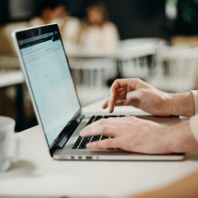 Close-up of hands typing on a laptop in a cozy indoor cafe setting.